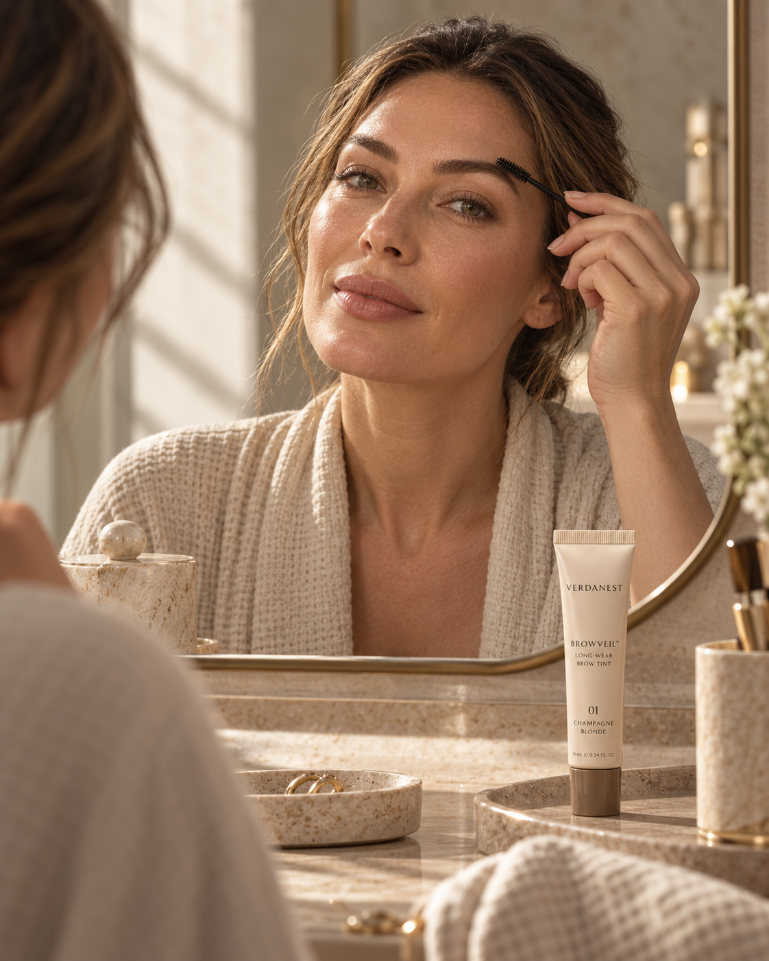 Woman gently grooming naturally defined brows at a warm sunlit vanity